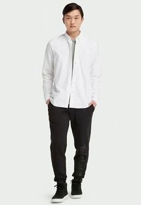 Camisa blanca de botones, camiseta gris debajo, pantalones negros con logo y zapatillas negras. Diseño minimalista, textura suave, ajuste casual.