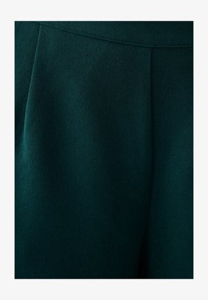 Tmavozelená tkanina, hladká textúra, so skrútenými detailmi pod pásom, vhodná na ušité nohavice alebo kalhoty.