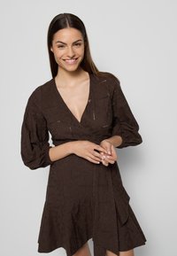 Brązowa sukienka haftowana z długimi bufkami i dekoltem w kształcie litery V, z kwiatowymi wzorami i subtelną teksturą na całej powierzchni.