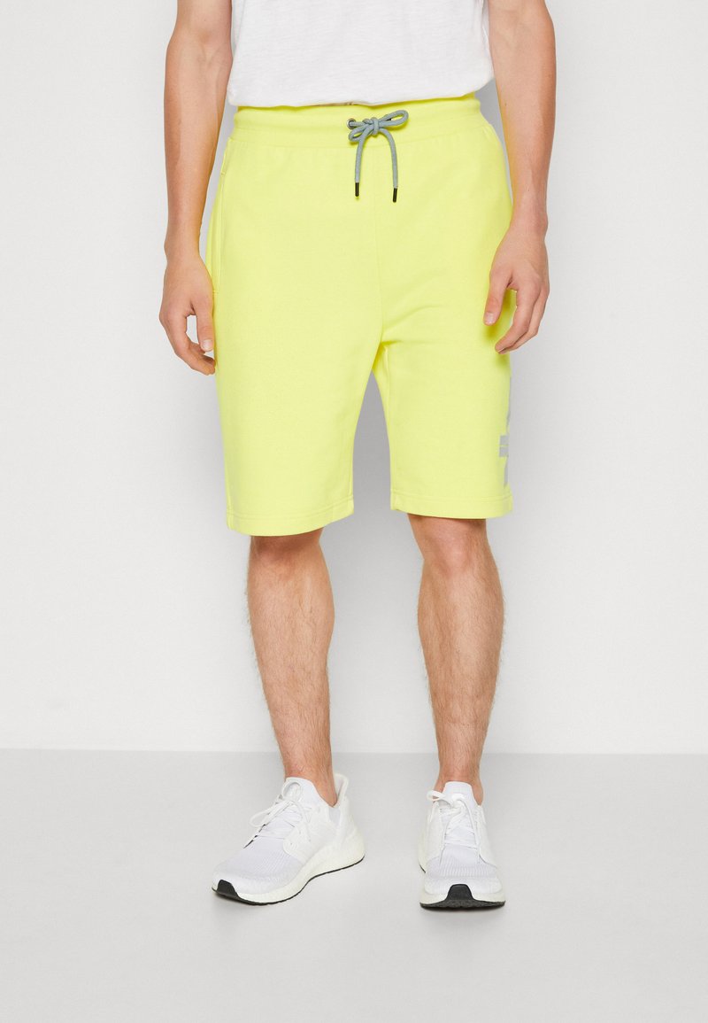 Neon-gelbe Sweatshorts mit einem elastischen Bund und grauem Kordelzug. Sie verfügen über Seitentaschen und ein dezentes Logodetail am linken Bein.