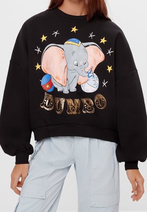 Osoba nosząca czarną bluzę z ilustracją słonia Dumbo trzymającego flagę, otoczona gwiazdami, a poniżej napis "DUMBO".