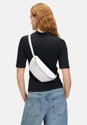 Weiße Leder-Crossbody-Tasche mit Reißverschluss, geschwungener Form und verstellbarem Trageriemen, getragen über einem schwarzen, figurbetonten Shirt, vor einem neutralen Hintergrund.