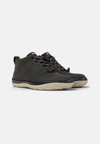 Botas de tobillo de cuero negro con cordones grises, suela de goma flexible y acabado mate suave. Marca roja en la lengüeta.
