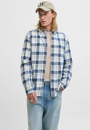 Geruite flanellen overhemd in blauw en wit, met een knoopsluiting aan de voorkant en lange mouwen. Draagt het over een beige t-shirt, gecombineerd met lichte denim.