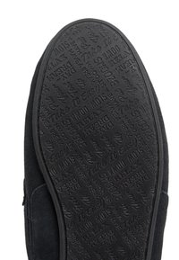 Svart mocka slip-on sko med en texturerad gummisula som har präglade mönster och fraser, inklusive "Ta det lugnt" och "Slappna av."