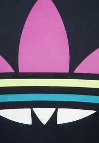 Svart textil med en stor grafisk design som har en rosa form ovanför gröna, blå och vita accenter. Ytan har en slät textur.