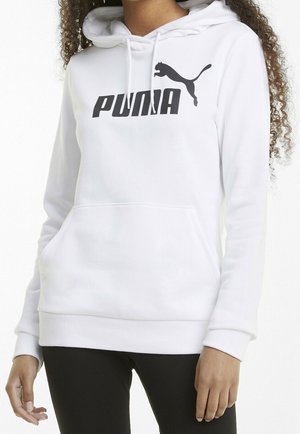 Sweat à capuche blanc avec logo Puma noir sur la poitrine porté par une personne aux cheveux bouclés, associé à un pantalon noir.