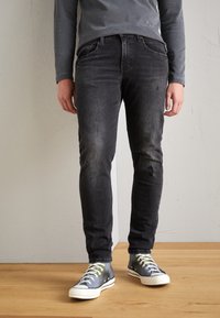 Svarta denimjeans med smal passform, med en blekt tvätt, knäskador och sydda bakfickor, tillsammans med blå sneakers.