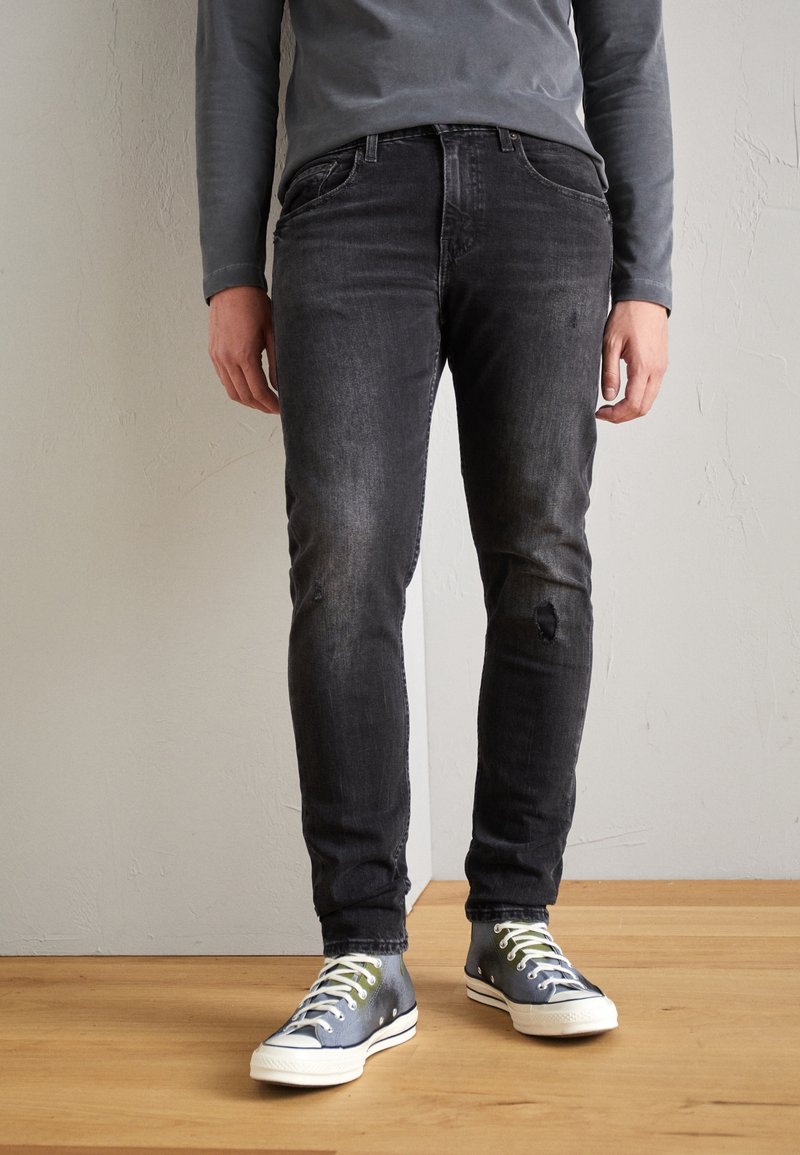 Svarta denimjeans med smal passform, med en blekt tvätt, knäskador och sydda bakfickor, tillsammans med blå sneakers.