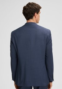 Marineblauer Anzugjacke im zweiteiligen Design mit texturiertem Finish, ausgestattet mit Reverskragen, doppeltem Rückenventil und geknöpften Manschetten. Die Rückansicht zeigt eine strukturierte Passform.