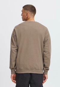 Brun bomullsgenser med rund hals, lange ermer og ribbestrikkede mansjetter. Designet har en avslappet passform og ensfarget tekstur, uten mønstre.