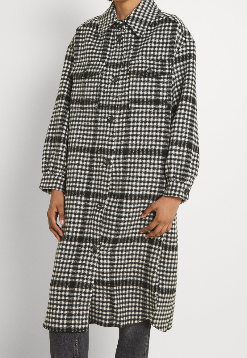 Přehledná černobílá oversized košile-jacket s knoflíky vpředu, dvěma náprsními kapsami a límcem. Vyrobena z měkké tkaniny.