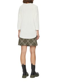 Langärmliges weißes Oberteil, Minirock aus olivgrünem Karostoff und schwarze Stiefeletten mit grünen Sohlen. Weicher Stoff und lockere Passform.