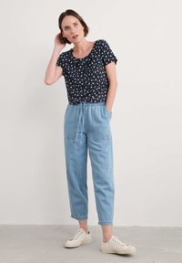 Tamsiai mėlynas gėlių motyvo trumpas rankovės viršus su apvaliu iškirpimu, derinamas su šviesiai mėlynomis siaurėjančiomis džinsinėmis kelnėmis, turinčiomis elastingą juosmenį ir šonines kišenes.