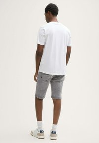 Weißes Kurzarm-T-Shirt, graue Denim-Shorts und weiße Sneakers mit navy farbigen Akzenten. Glatter Stoff mit minimalistischem Design.
