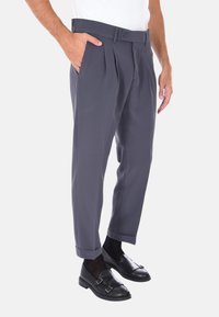 Pantaloni grigi a pieghe con una vestibilità affusolata, dotati di chiusura con bottone, tasche laterali e orli arrotolati, abbinati a scarpe in pelle nere.