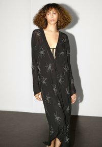 Černé dlouhé šaty z průhledné látky se stříbrnou květinovou výšivkou. Mají hluboký výstřih do véčka, dlouhé rukávy a zavazování na hrudi.