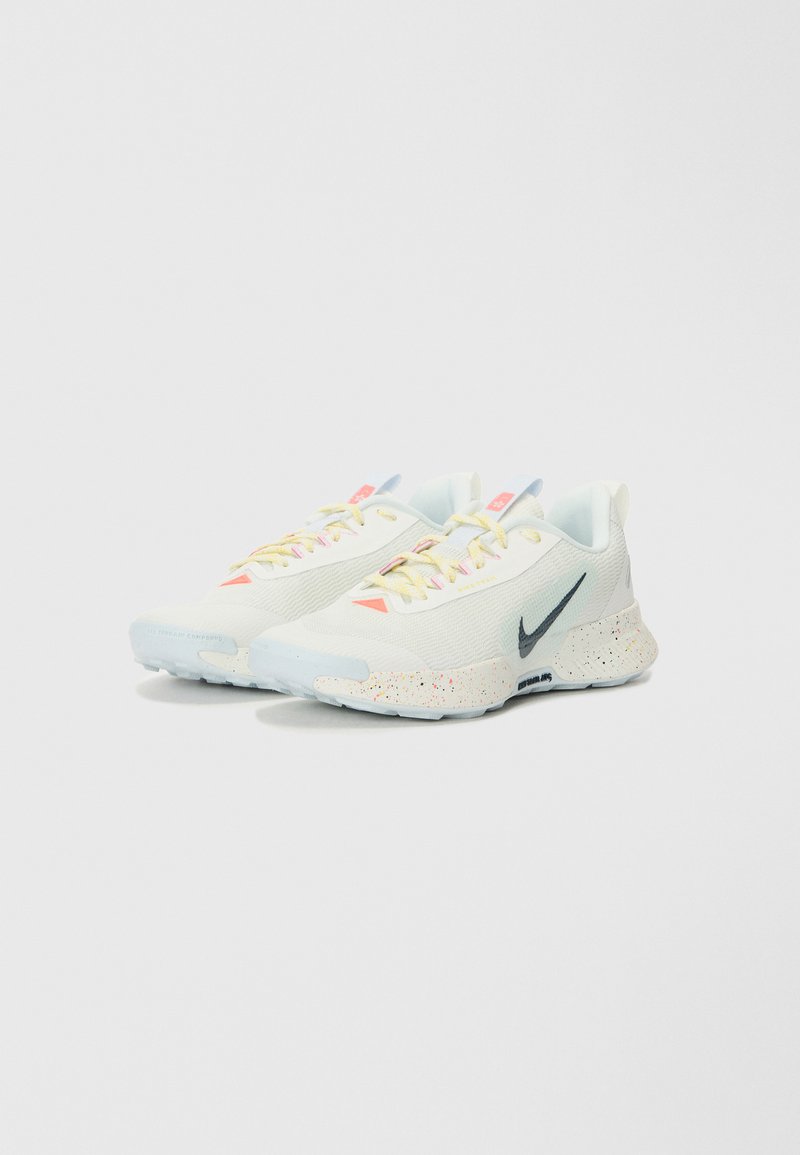 Zapatillas deportivas blancas con parte superior de malla, suela salpicada de colores y un swoosh negro en contraste. Presenta cordones y acentos de color amarillo claro.