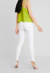 Top corto verde lima con tirantes finos, combinado con jeans blancos ajustados y tacones altos blancos con un patrón de lunares.