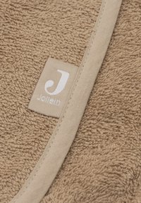 Tissu en éponge beige avec un bord cousu et une petite étiquette en tissu montrant un "J" blanc et le texte "Jollein".