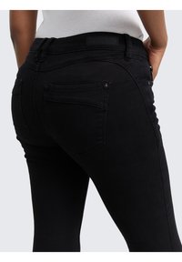 Czarne dżinsy z denimu o dopasowanym kroju, wyposażone w dwie tylne kieszenie i teksturowaną powierzchnię. Pas ma skórzaną naszywkę z logo marki.
