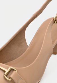 Μπεζ γυναικείο παπούτσι με ψηλό τακούνι από λείο υλικό, με λεπτομέρεια χρυσής αγκράφας και ανοιχτή σχεδίαση πίσω, με μαλακό, υφασμένο εσωτερικό πάτο.