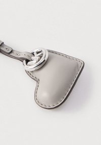 Γκρι δερμάτινο μπρελόκ σε σχήμα καρδιάς με εμφανείς ραφές και ασημένιο κυκλικό μεταλλικό στοιχείο. Λεία υφή και μινιμαλιστικός σχεδιασμός.