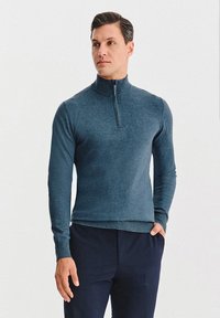 Ciemnoniebieski, zapinany sweter z wysokim kołnierzem, wykonany z miękkiego materiału, z długimi rękawami i dopasowanym krojem dla uzyskania smukłego wyglądu.