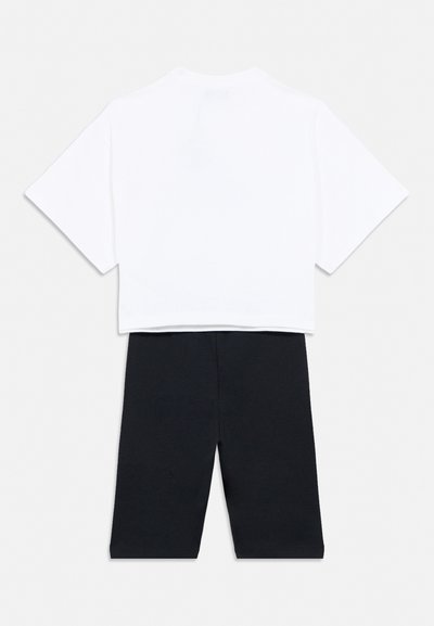 Λευκό κοντομάνικο crop top συνδυασμένο με μαύρο σορτς μήκους μέχρι το γόνατο, τοποθετημένα επίπεδα σε ανοιχτό γκρι φόντο.