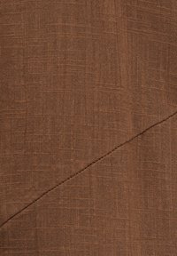 Tissu marron texturé avec un motif de tissage visible et une couture diagonale traversant la partie inférieure du matériau.