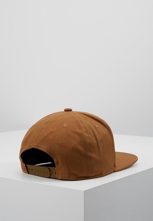 Braune Baseballkappe mit flachem Schirm und verstellbarem Snapback-Verschluss, sitzt auf einer weißen Oberfläche vor einem schlichten hellen Hintergrund.