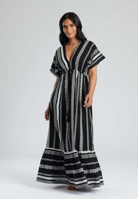 Abito maxi a righe bianche e nere con maniche corte, scollatura a V e gonna fluida che presenta intricati motivi decorativi vicino all'orlo.