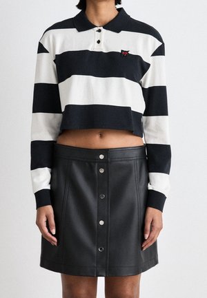 Persoon draagt een zwart-wit gestreepte cropped polo met lange mouwen en een zwarte, hooggesneden A-lijn rok met knopen aan de voorkant.