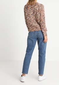 Barevný pletený svetr s volným střihem, ribonovaným lemem a kulatým výstřihem, spárovaný se světle modrými zúženými džíny a bílými teniskami.