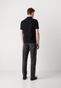 Black polo shirt with short sleeves, paired with dark grey jeans. Visible stitching on jeans and smooth fabric texture of the polo.