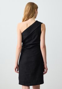 Abito in lino nero con design a spalla unica, forma aderente e una texture morbida. Dettagli delle cuciture lungo la vita aggiungono interesse visivo.