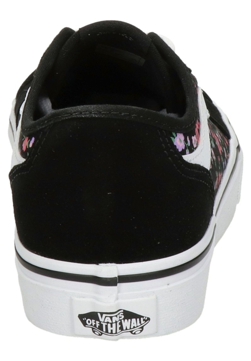 Vista trasera de una zapatilla negra Vans con suela blanca, franja lateral blanca y pequeños patrones florales en rosa y púrpura cerca del talón.