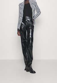 Pantaloni alti in vernice nera abbinati a un blazer a scacchi bianco e nero, con una silhouette aderente e un design strutturato.