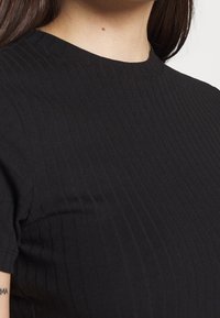 Schwarzes geripptes T-Shirt mit rundem Halsausschnitt und kurzen Ärmeln. Der Stoff ist strukturiert und zeigt ein slim fit Design.