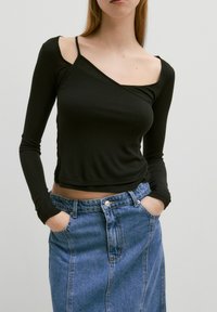 Schwarzes, geripptes Langarmoberteil mit schulterfreier Gestaltung. Kombiniert mit einem verwaschenen blauen Jeansrock mit Fronttaschen und Knopfverschluss.