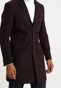 Abrigo de lana burdeos con un diseño entallado, cuello con muescas y dos botones. Cuenta con bolsillos laterales y una textura suave, adecuado para ocasiones formales.