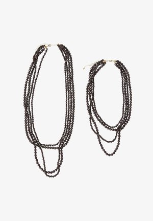 To-lagede halskæder med mørke runde perler, i varierende længder, afsluttet med guldfarvet hardware og kædeforlængelser.