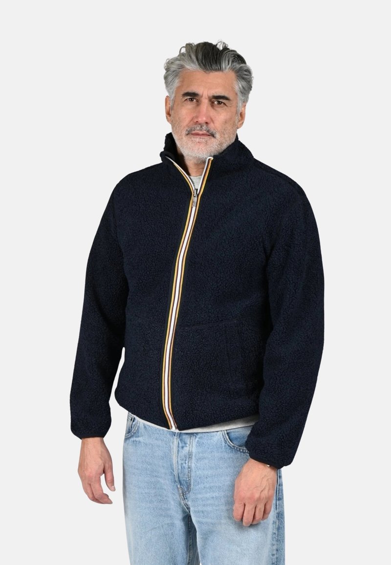 Giacca in pile blu navy con collo alto, cerniera integrale e dettagli a righe color crema, oro e ruggine; due tasche frontali, tessuto strutturato.