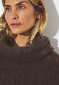 Ruskea ribattukuvioinen korkeakauluksinen neulepaita, valmistettu pehmeästä materiaalista, jossa on kääntyvä kaulus ja tekstuuri pinta. Minimalistinen muotoilu ja tiukka istuvuus.
