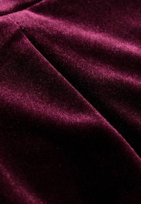 Dyb bordeaux velourstof med en blød, glat tekstur, der har en subtil glans og foldede områder, som skaber dybde og bevægelse.