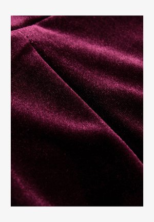 Dyb bordeaux velourstof med en blød, glat tekstur, der har en subtil glans og foldede områder, som skaber dybde og bevægelse.