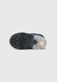 Suela de zapato con goma negra texturizada, dibujo de banda de rodadura para tracción y una sección de goma clara que revela el acolchado. Presenta elementos adicionales de agarre.