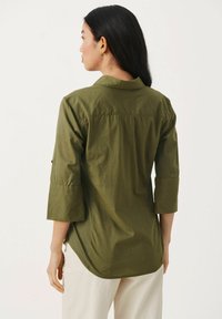 Camicia verde oliva con maniche a tre quarti, polsini abbottonati, colletto e orlo arrotondato. Il tessuto sembra leggero con una sottile texture.