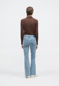 Dugotrajna majica smeđe boje s rebrastim uzorkom i svijetloplavim trapezastim trapericama. Odjeća ima usku siluetu i detalj stražnjeg džepa.