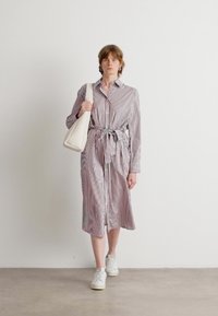 Abito a righe in tessuto leggero con vita impostata, dotato di maniche lunghe e chiusura a bottoni davanti. Abbinato a una borsa a spalla bianca e sneakers.